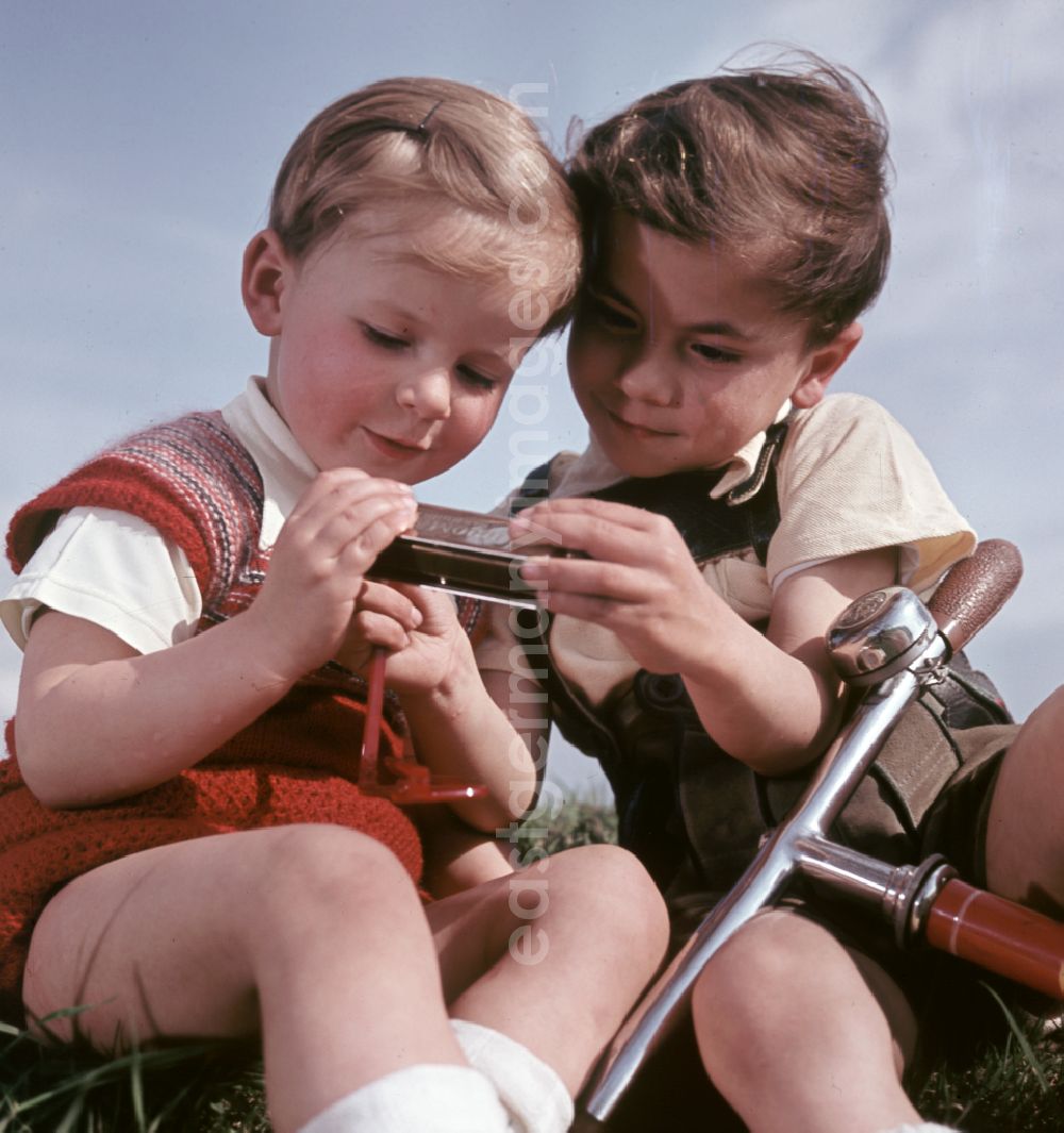 Coswig: Two boys play with a harmonica and a scooter in Coswig, Saxony in the territory of the former GDR, German Democratic Republic