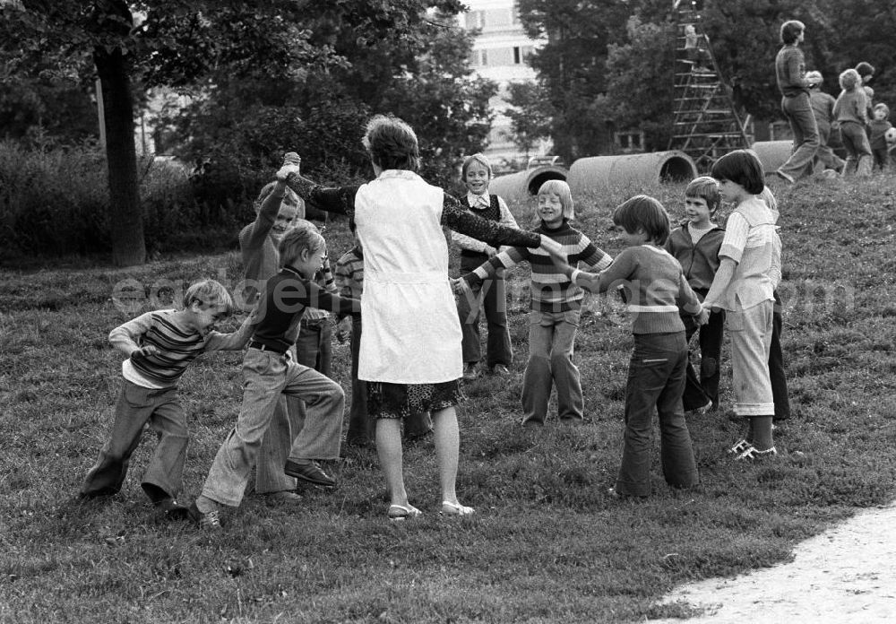 GDR image archive: Berlin - Kinder spielen auf einer Wiese neben einem Spielplatz im Neubaugebiet mit einer Erzieherin ein Kreisspiel.