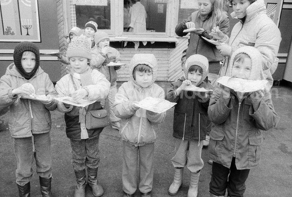 GDR photo archive: Berlin - Children eat full pancakes on the Berlin Christmas fair in Berlin, the former capital of the GDR, German democratic republic. Today there stands at this point the shopping centre Alexa