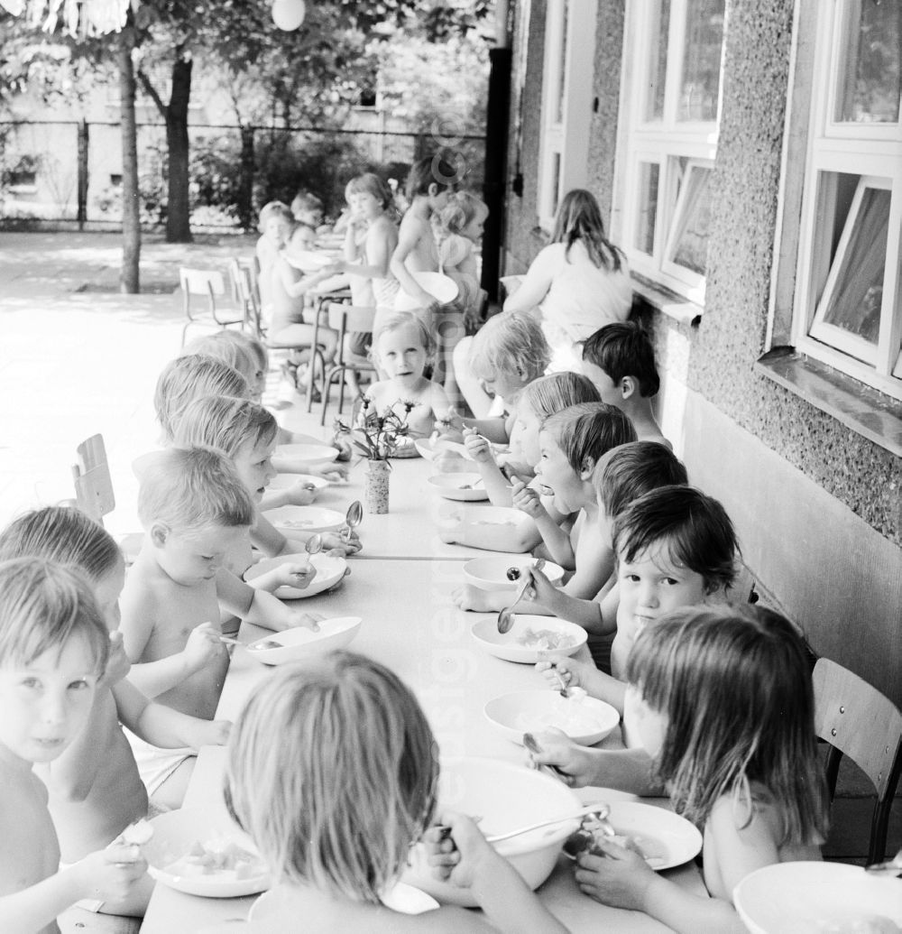 GDR picture archive: Berlin - Children celebrate the International Children's Day at a preschool in Berlin, the former capital of the GDR, German Democratic Republic. On this day there was always a festive program which consisted of sport and play. Here the Community lunch on the terrace