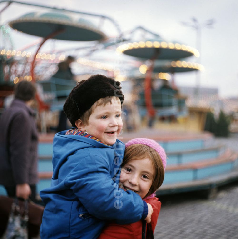 GDR photo archive: Berlin - Zwei Kinder amüsieren sich auf dem Weihnachtsmarkt am Berliner Alexanderplatz - hier hebt ein Mädchen lachend ihren kleinen Bruder auf den Arm.