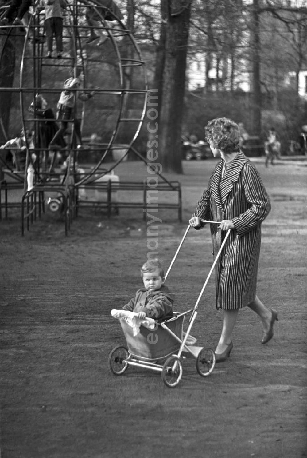 GDR picture archive: Leipzig - Eine Frau geht mit ihrem Kind in einem Sport-Kinderwagen Marke Eigenbau im Clara-Zetkin-Park in Leipzig spazieren, im Hintergrund spielen Kinder auf einem Klettergerüst.