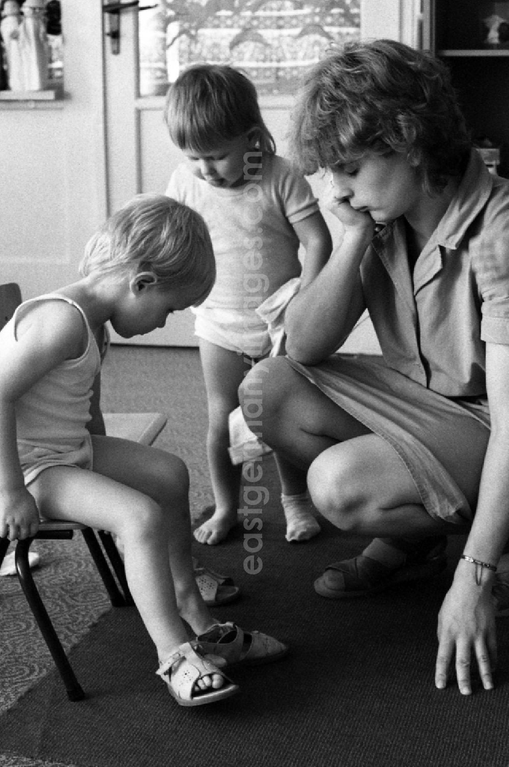 GDR photo archive: Berlin - Preparing for a nap in the kindergarten in Berlin Eastberlin on the territory of the former GDR, German Democratic Republic. Educator watching a toddler trying to undress on her own