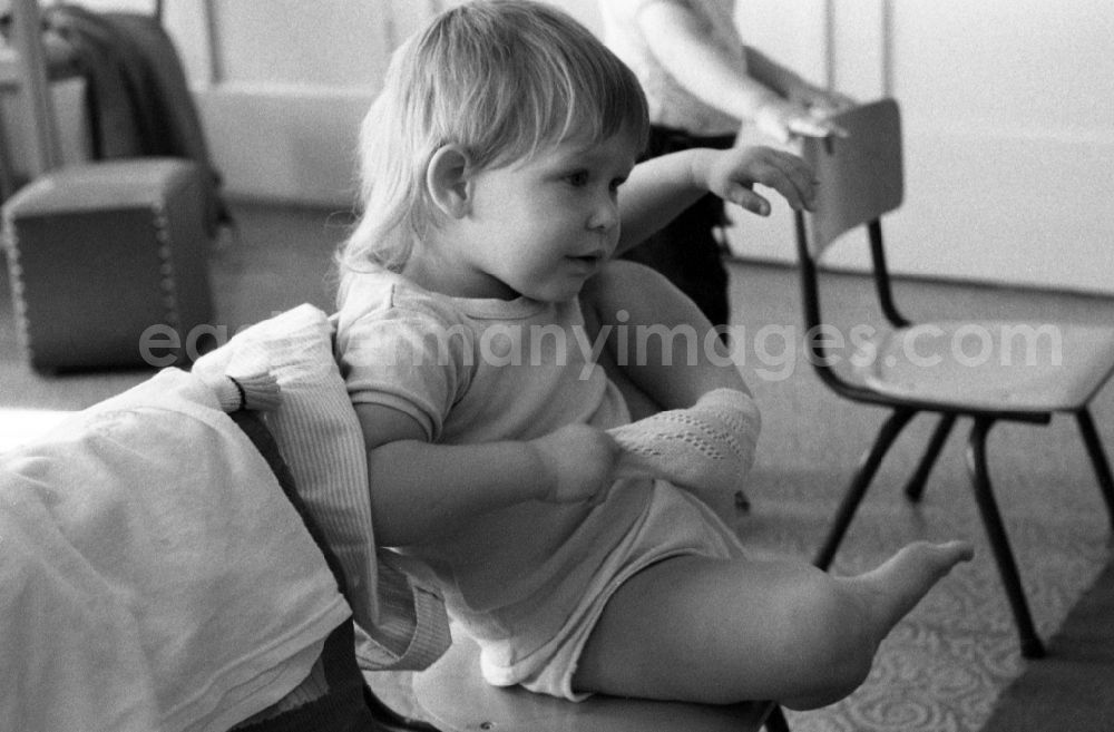 Berlin: Preparing for a nap in the kindergarten in Berlin Eastberlin on the territory of the former GDR, German Democratic Republic. Toddler tries to undress on his own and takes off a sock or stocking in the process