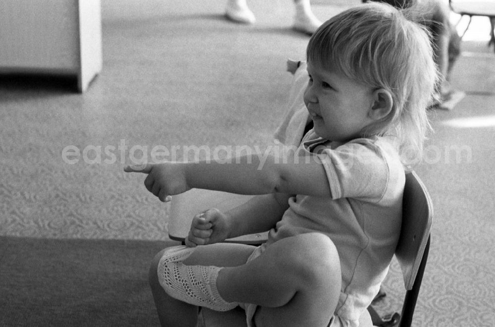 GDR image archive: Berlin - Preparing for a nap in the kindergarten in Berlin Eastberlin on the territory of the former GDR, German Democratic Republic. Toddler tries to undress on his own and takes off a sock or stocking in the process