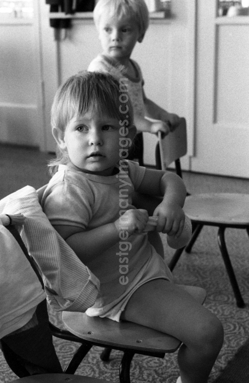 GDR image archive: Berlin - Preparing for a nap in the kindergarten in Berlin Eastberlin on the territory of the former GDR, German Democratic Republic. Toddler tries to undress on his own and pulls on his sock or stocking