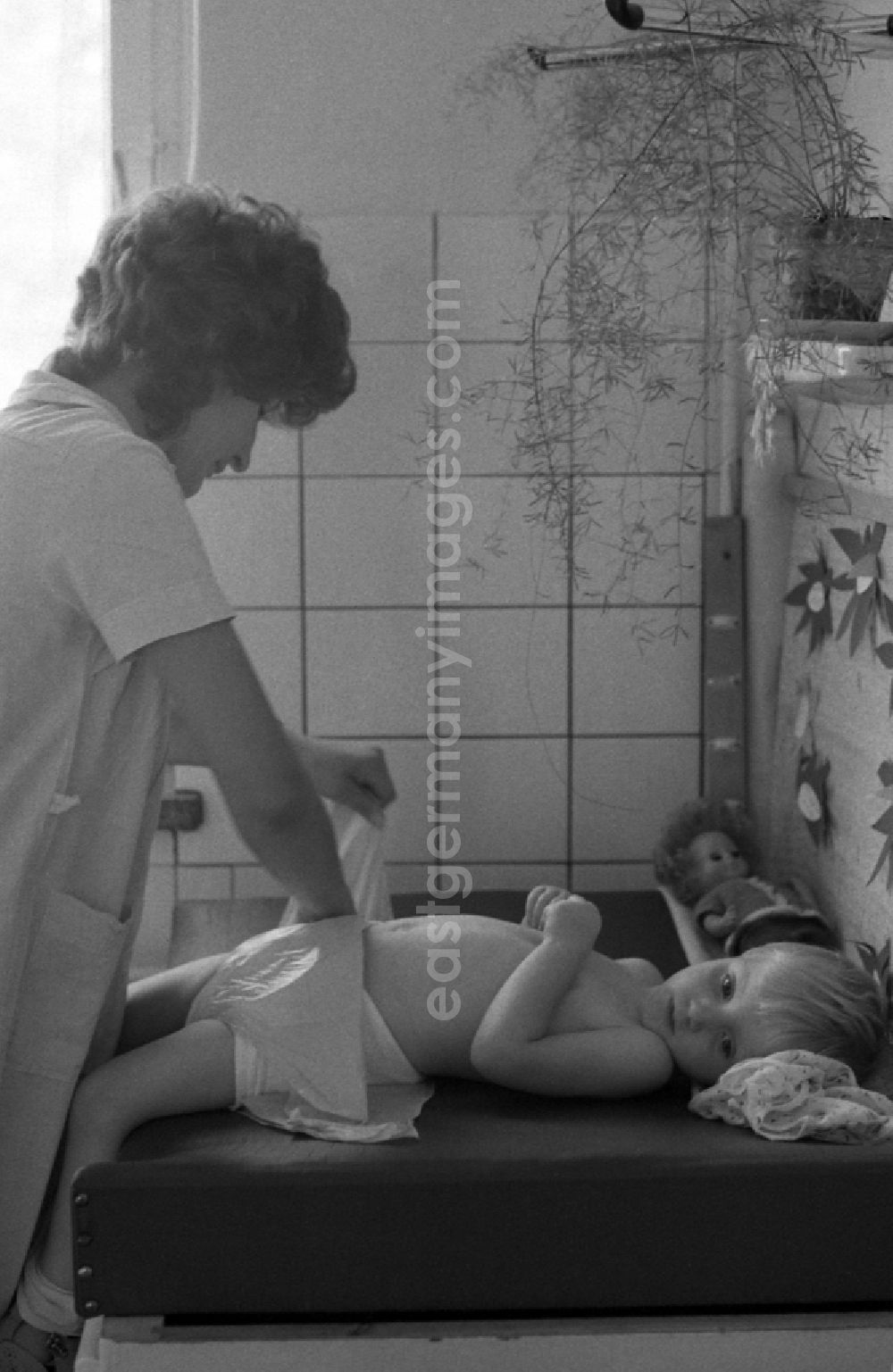 GDR picture archive: Berlin - Nursery nurse in a day nursery swaddles a toddler in Berlin Eastberlin on the territory of the former GDR, German Democratic Republic