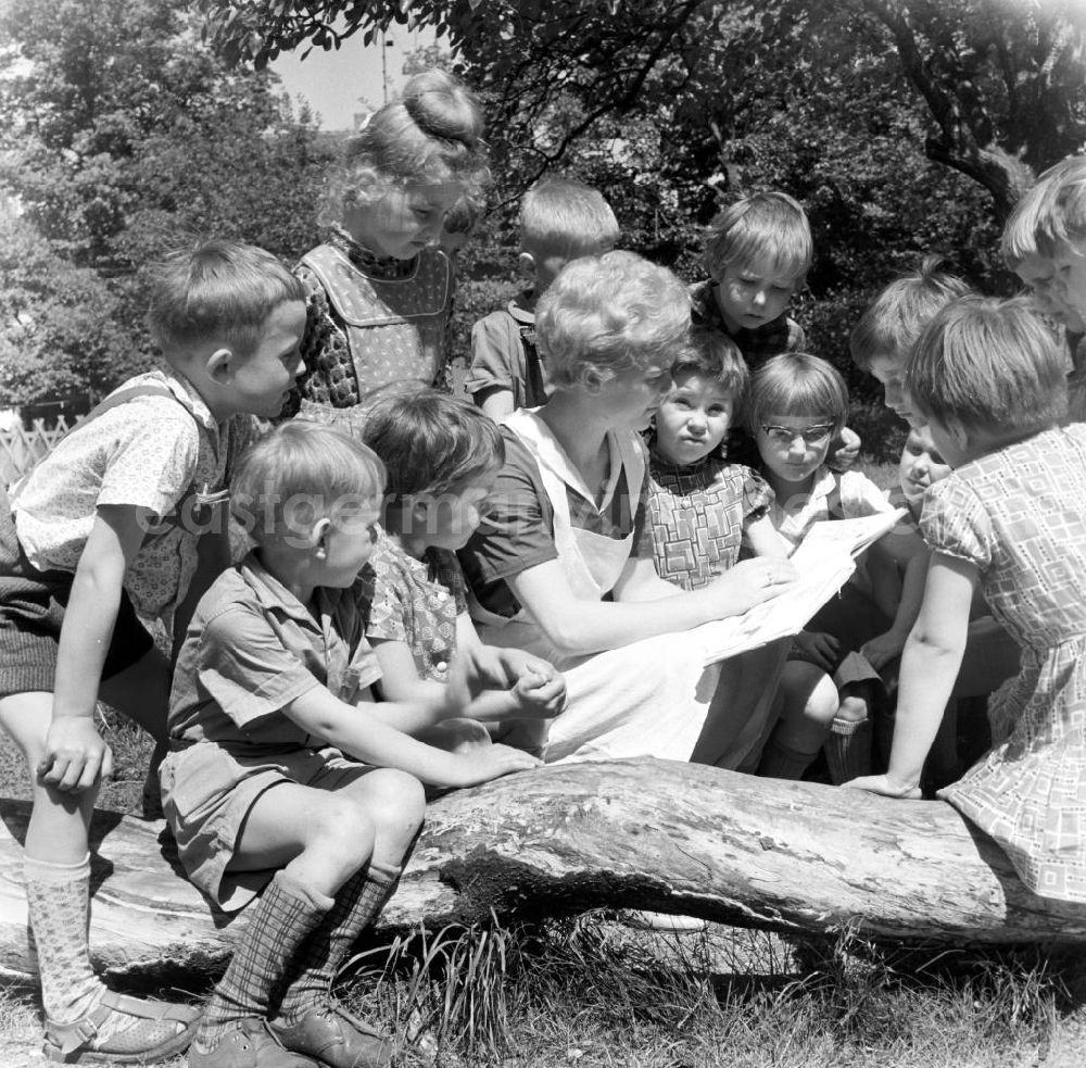 GDR picture archive: Brandenburg - Erzieherin und Kinder / Kleinkinder aus Kindergarten / Kita sitzen zusammen. Erzieherin liest aus einem Buch vor.
