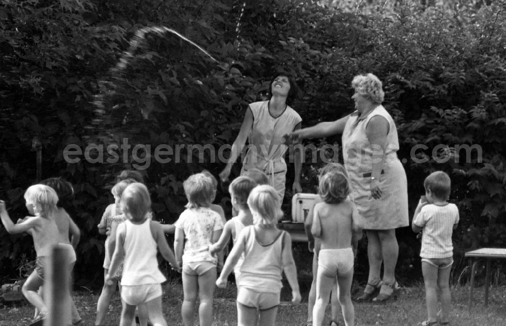 GDR picture archive: Berlin - Children in the garden of the kindergarten in summer in Berlin Eastberlin on the territory of the former GDR, German Democratic Republic. Nursery nurse spray water into the air for refreshment