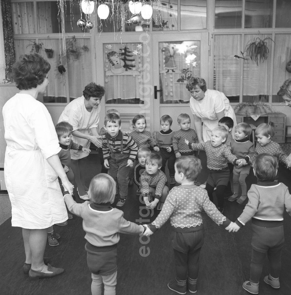 GDR picture archive: Silbitz - Everyday life in a baby cot in Silbitz in today s state of Thuringia. Children standing togetherwith nursery nurse in white coats in a circle