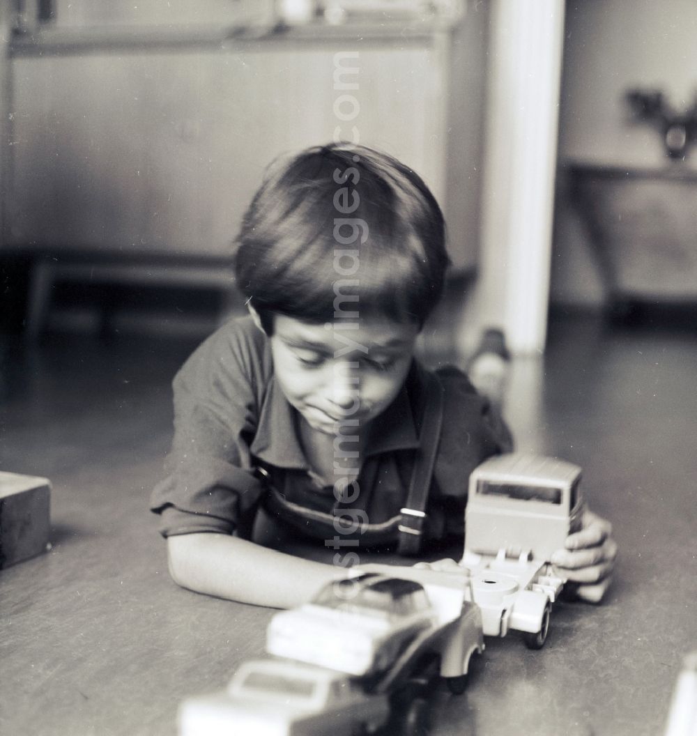 GDR image archive: Berlin - A small boy with leather trousers plays by his toys cars on the floor in Berlin, the former capital of the GDR, German democratic republic