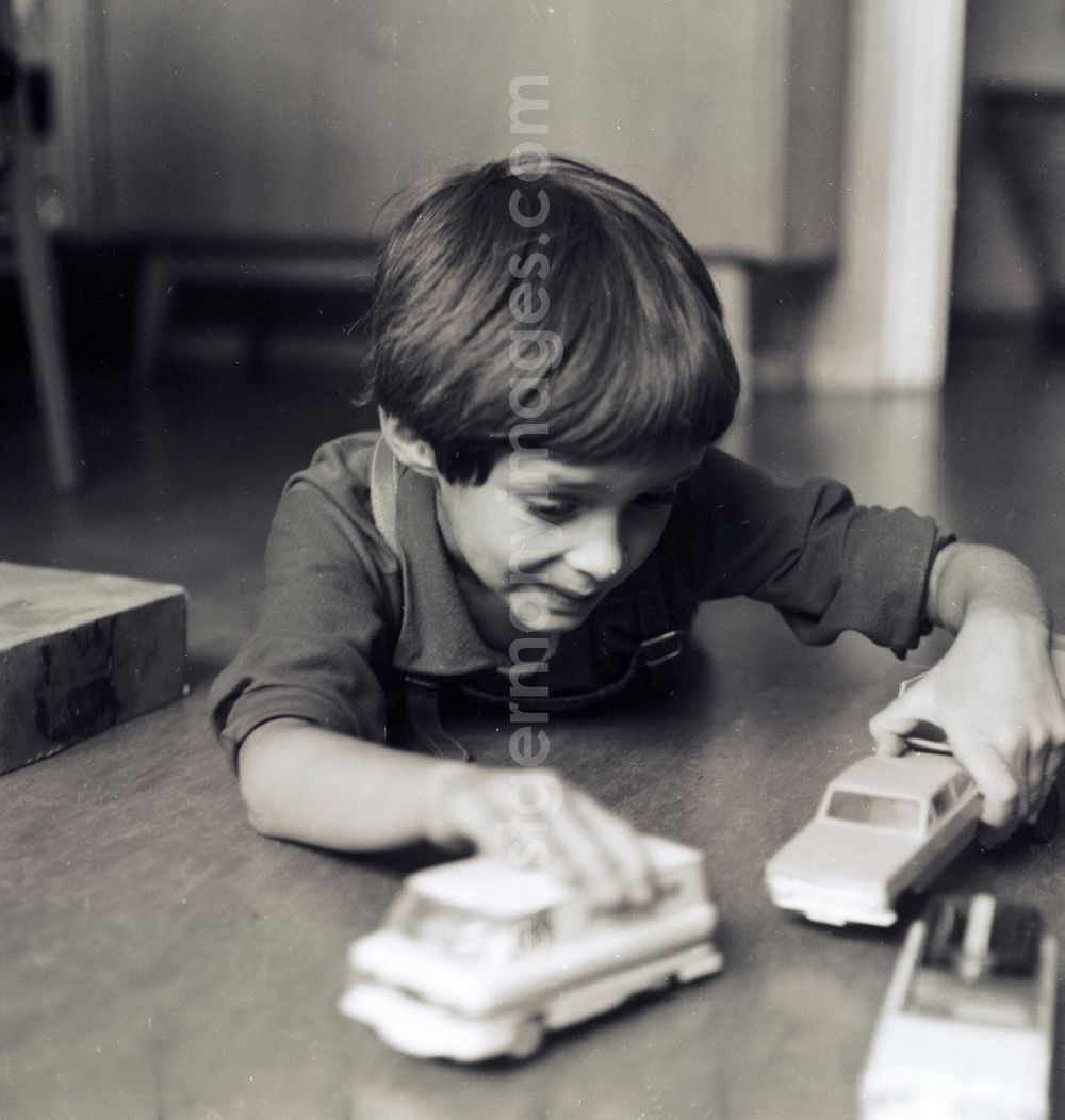 GDR photo archive: Berlin - A small boy with leather trousers plays by his toys cars on the floor in Berlin, the former capital of the GDR, German democratic republic