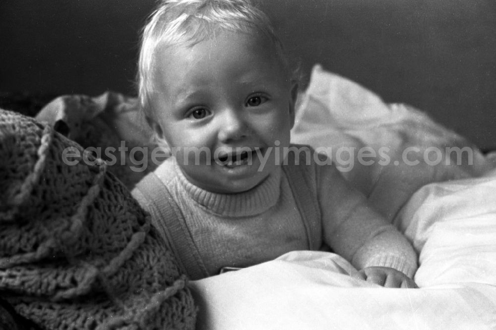 GDR image archive: Merseburg - A small laughing boy sits in his little bed in Merseburg in the federal state Saxony-Anhalt in Germany