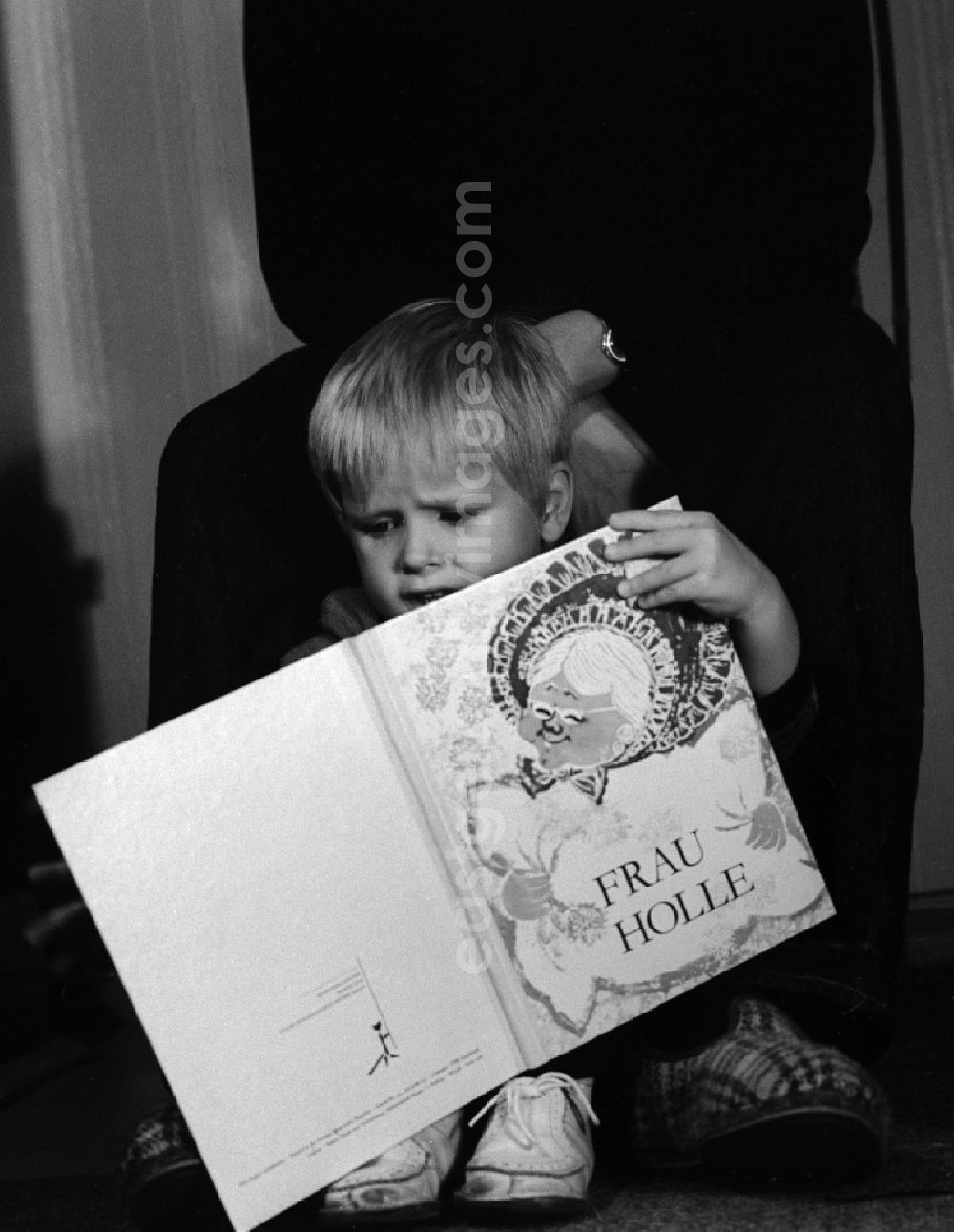 GDR image archive: Berlin - A small child is sitting between the feet of an adult and looks the children's book Mother Holle on, in Berlin, the former capital of the GDR, German Democratic Republic