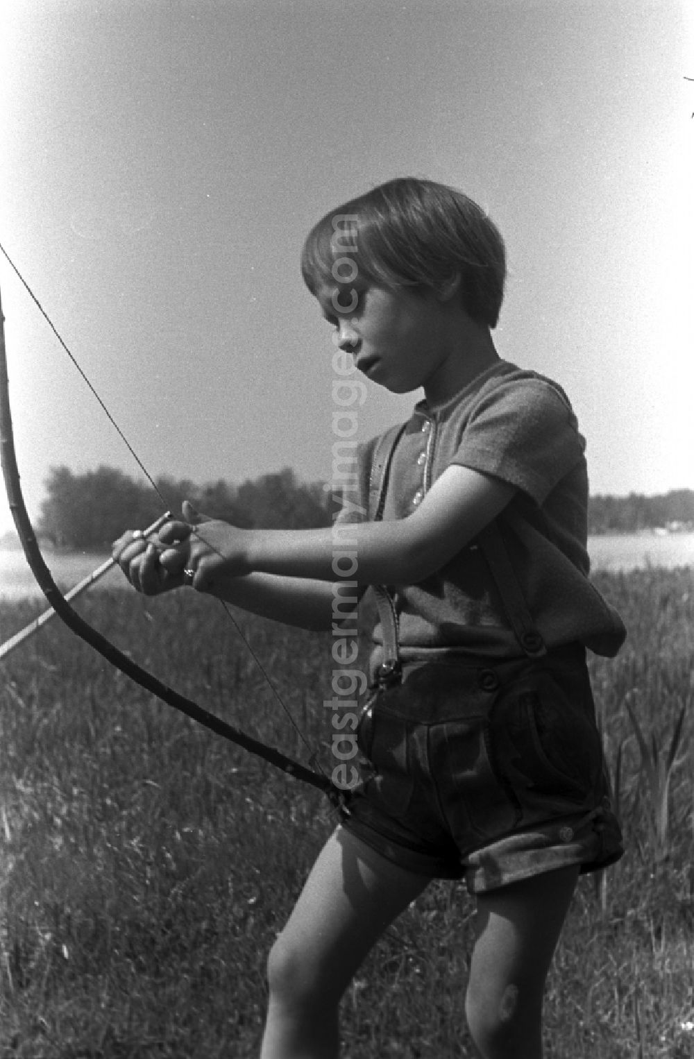 GDR photo archive: Kirchmöser - A small child in leather pants playing with bow and arrow on a meadow in Brandenburg
