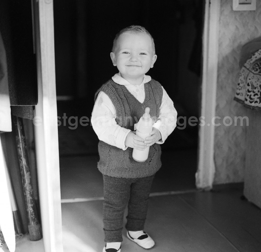 GDR picture archive: Mittenwalde - A small child holding a feeding bottle in his hands in Mittenwalde in Brandenburg on the territory of the former GDR, German Democratic Republic