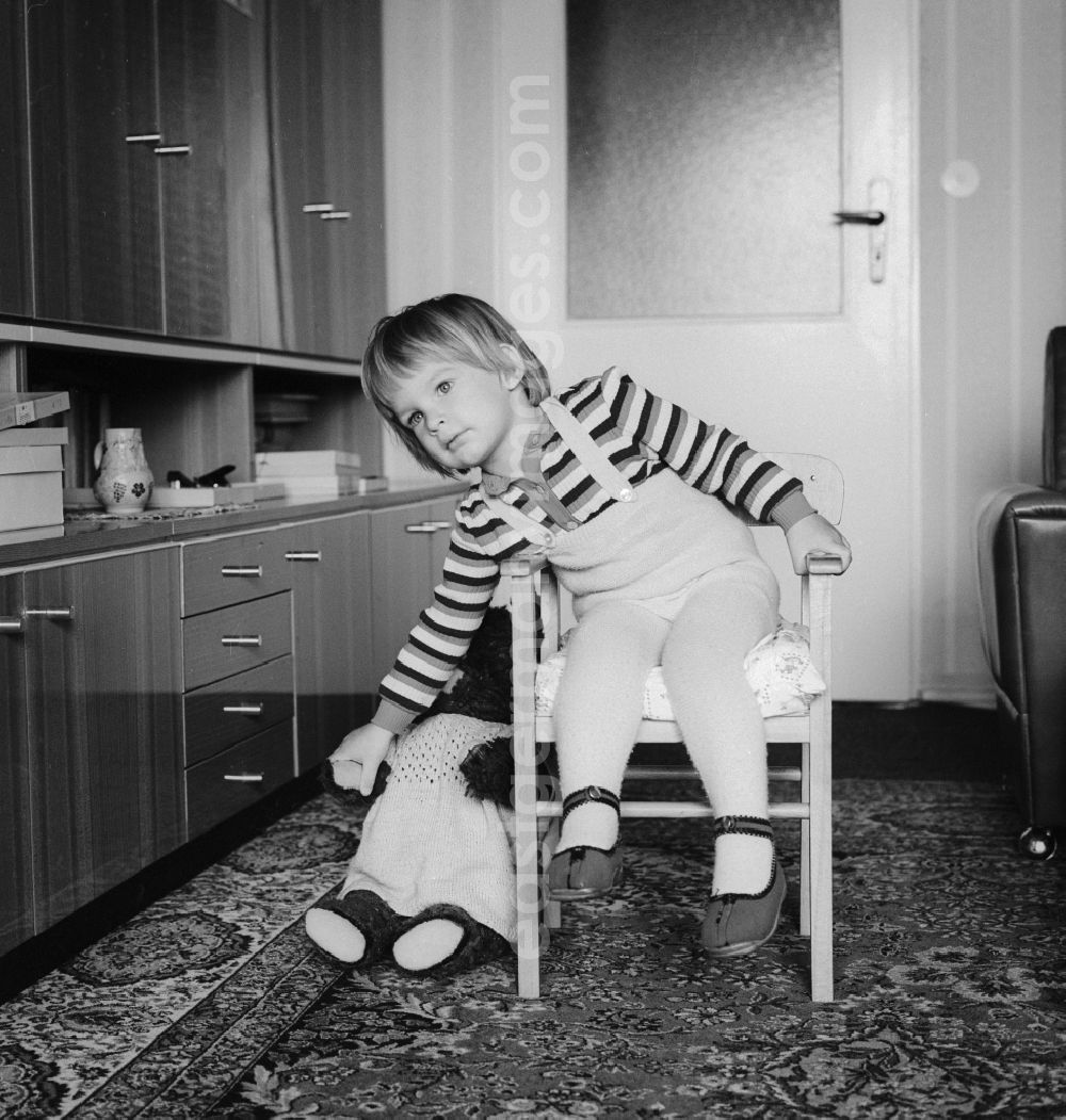 GDR picture archive: Berlin - Cute little baby sitting dreamily on a chair and grabs his toy in Berlin