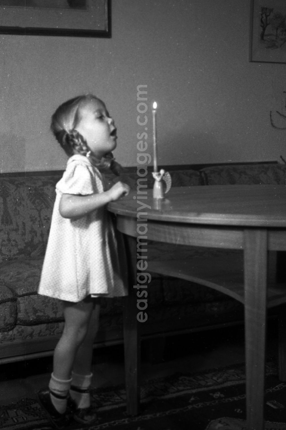 GDR photo archive: Merseburg - A small girl with plaits tries to blow out a candle which stands on the table, in Merseburg in the federal state Saxony-Anhalt in Germany