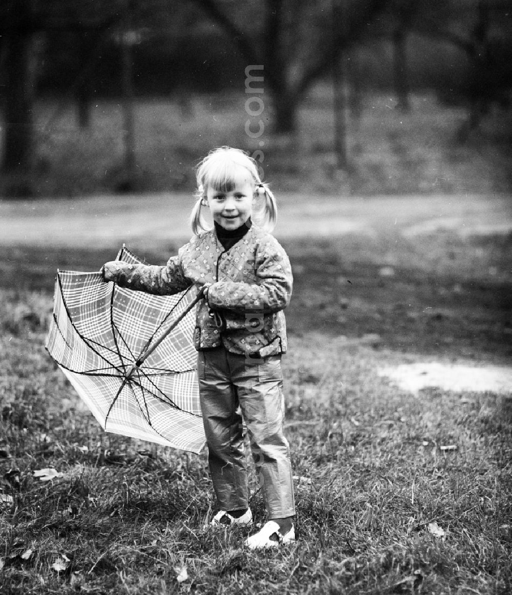 GDR photo archive: Berlin - A small girl with plaits stands with an umbrella on a meadow in Berlin, the former capital of the GDR, German democratic republic