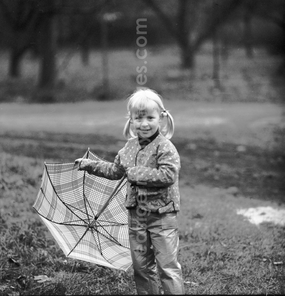 GDR picture archive: Berlin - A small girl with plaits stands with an umbrella on a meadow in Berlin, the former capital of the GDR, German democratic republic