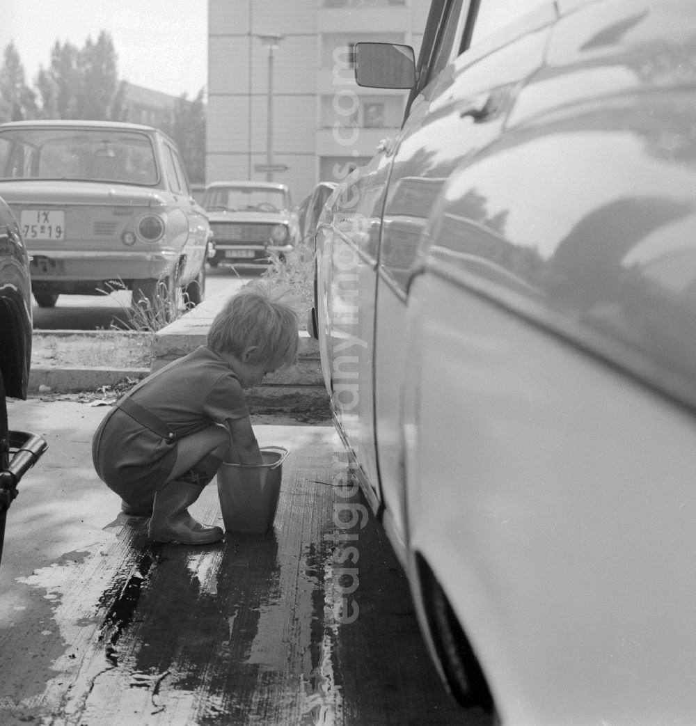 GDR photo archive: Berlin - A toddler with rubber boots and bucket at the car wash in a parking lot in Berlin, the former capital of the GDR, the German Democratic Republic
