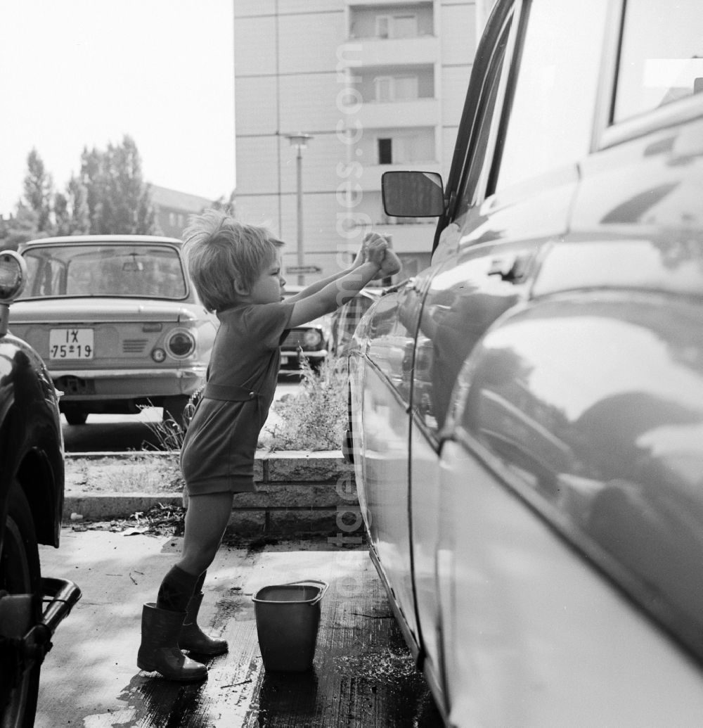 Berlin: A toddler with rubber boots and bucket at the car wash in a parking lot in Berlin, the former capital of the GDR, the German Democratic Republic