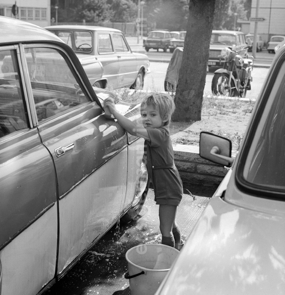 GDR photo archive: Berlin - A toddler with rubber boots and bucket at the car wash in a parking lot in Berlin, the former capital of the GDR, the German Democratic Republic