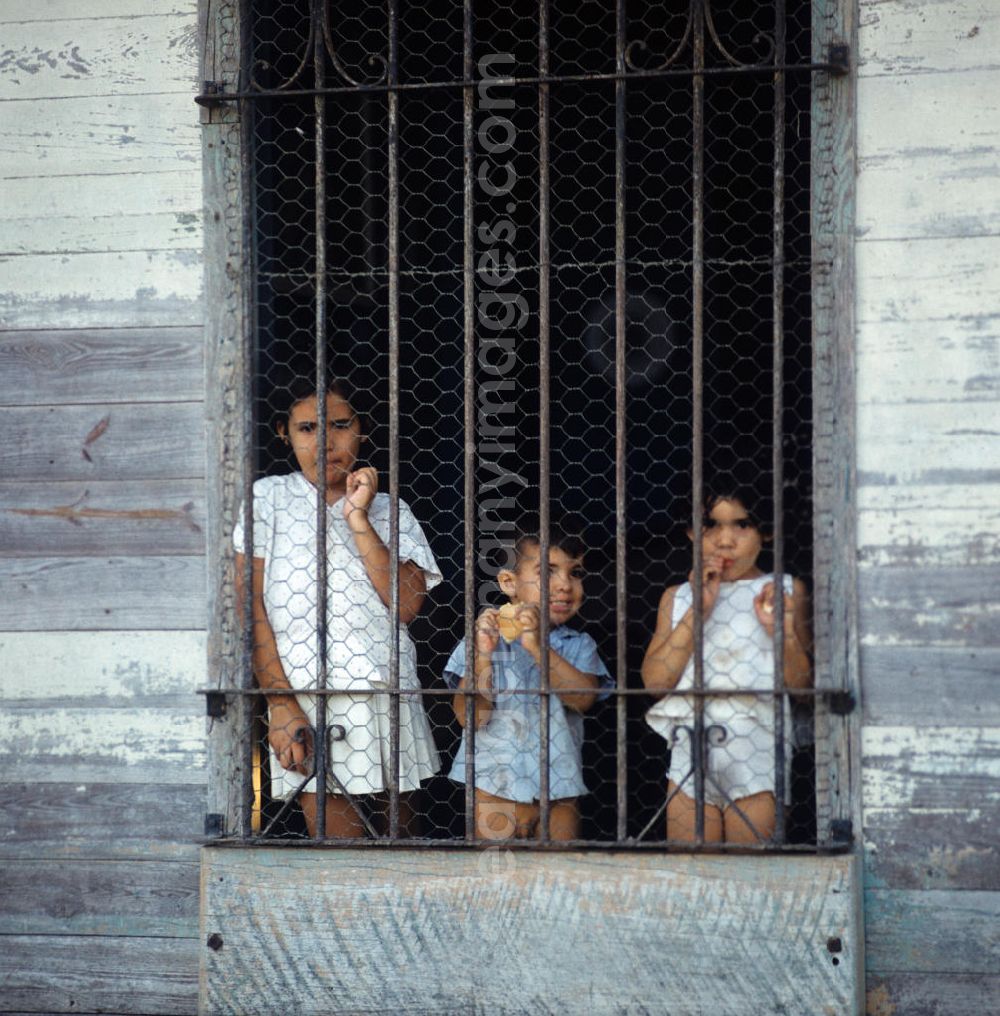 GDR picture archive: Nuevitas - Drei Kinder blicken neugierig durch ein vergittertes Fenster in einem Haus in der kubanischen Hafenstadt Nuevitas. Children at the window in the port city Nuevitas.