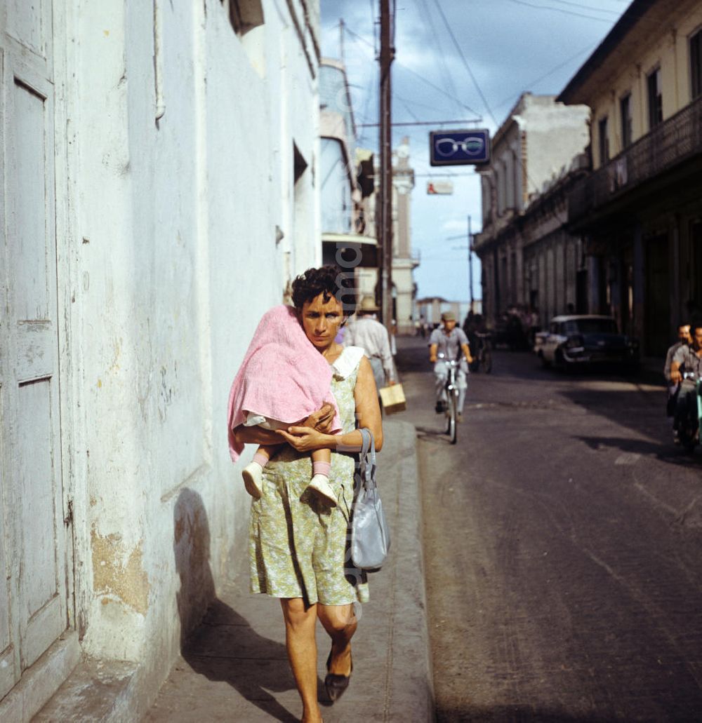 Santa Clara: Straßenszene in Santa Clara in Kuba - eine Mutter läuft mit ihrem kleinen Kind auf dem Arm die Straße entlang. Street scene in Santa Clara - Cuba.