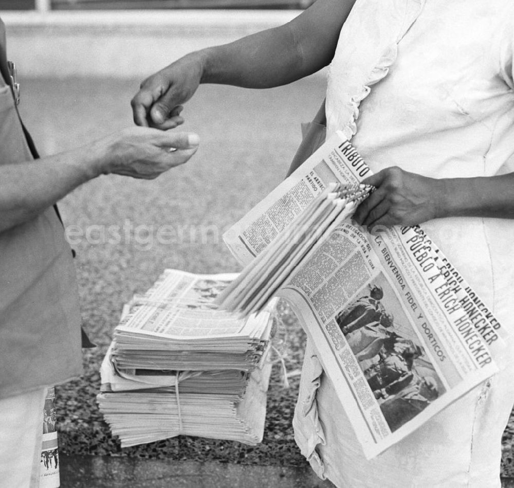 GDR photo archive: Havanna - Ein Passant kauft bei einer Zeitungsverkäuferin auf einer Straße in Havanna die aktuelle Ausgabe der Granma, der offiziellen Zeitung der Kommunistischen Partei Kubas (PCC). Die Zeitung zeigt ein Foto von der Ankunft des Staats- und Parteivorsitzenden der DDR, Erich Honecker, der vom 2