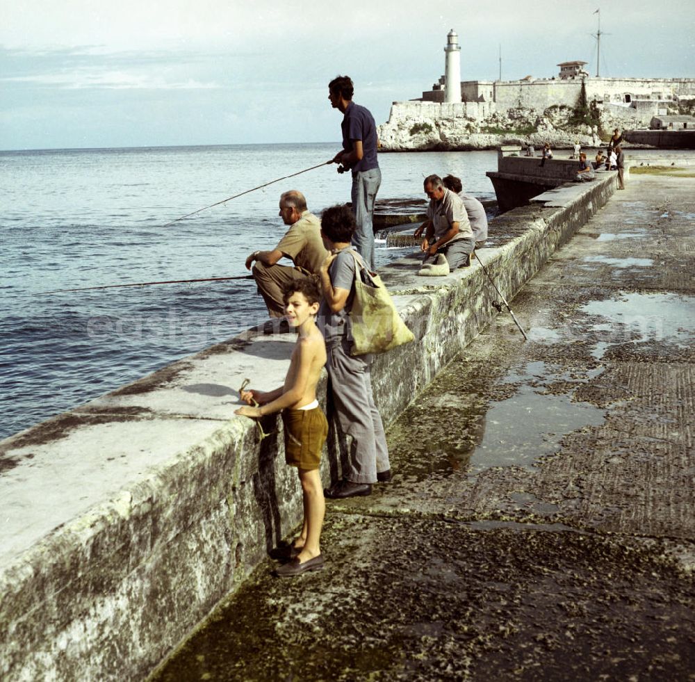 GDR picture archive: Havanna - Angler sitzen auf der Mauer an der acht Kilometer langen Uferpromenade, dem sogenannten Malecón in Havanna. Im Hintergrund die historische Festung El Morro, eines der Wahrzeichen der kubanischen Hauptstadt.