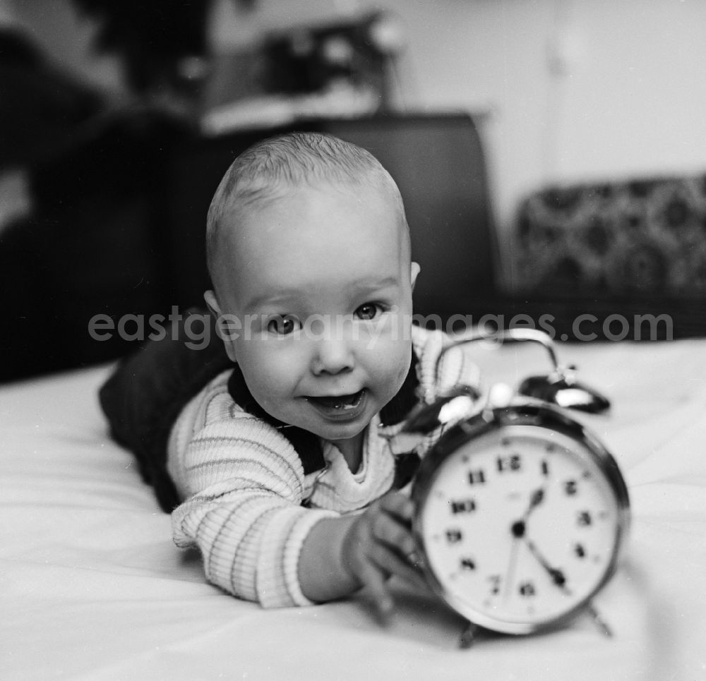 GDR photo archive: Berlin - Laughing toddler with dungarees playing on a playmat with an alarm clock in Berlin, the former capital of the GDR, the German Democratic Republic