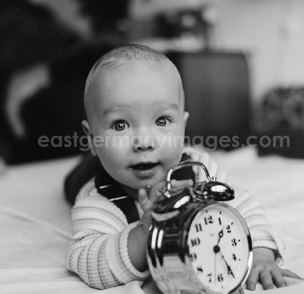 GDR picture archive: Berlin - Laughing toddler with dungarees playing on a playmat with an alarm clock in Berlin, the former capital of the GDR, the German Democratic Republic