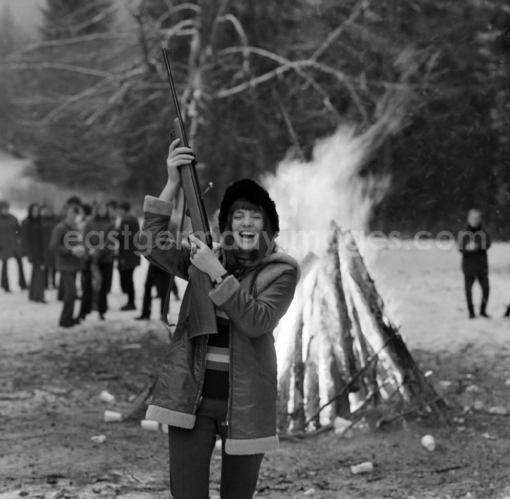 GDR image archive: Schmiedefeld am Rennsteig - A woman holds up an air rifle while a campfire burns in the background. She is a member of the Polish Landjugend, which is on a trip to Schmiedefeld am Rennsteig on the territory of the former GDR, German Democratic Republic