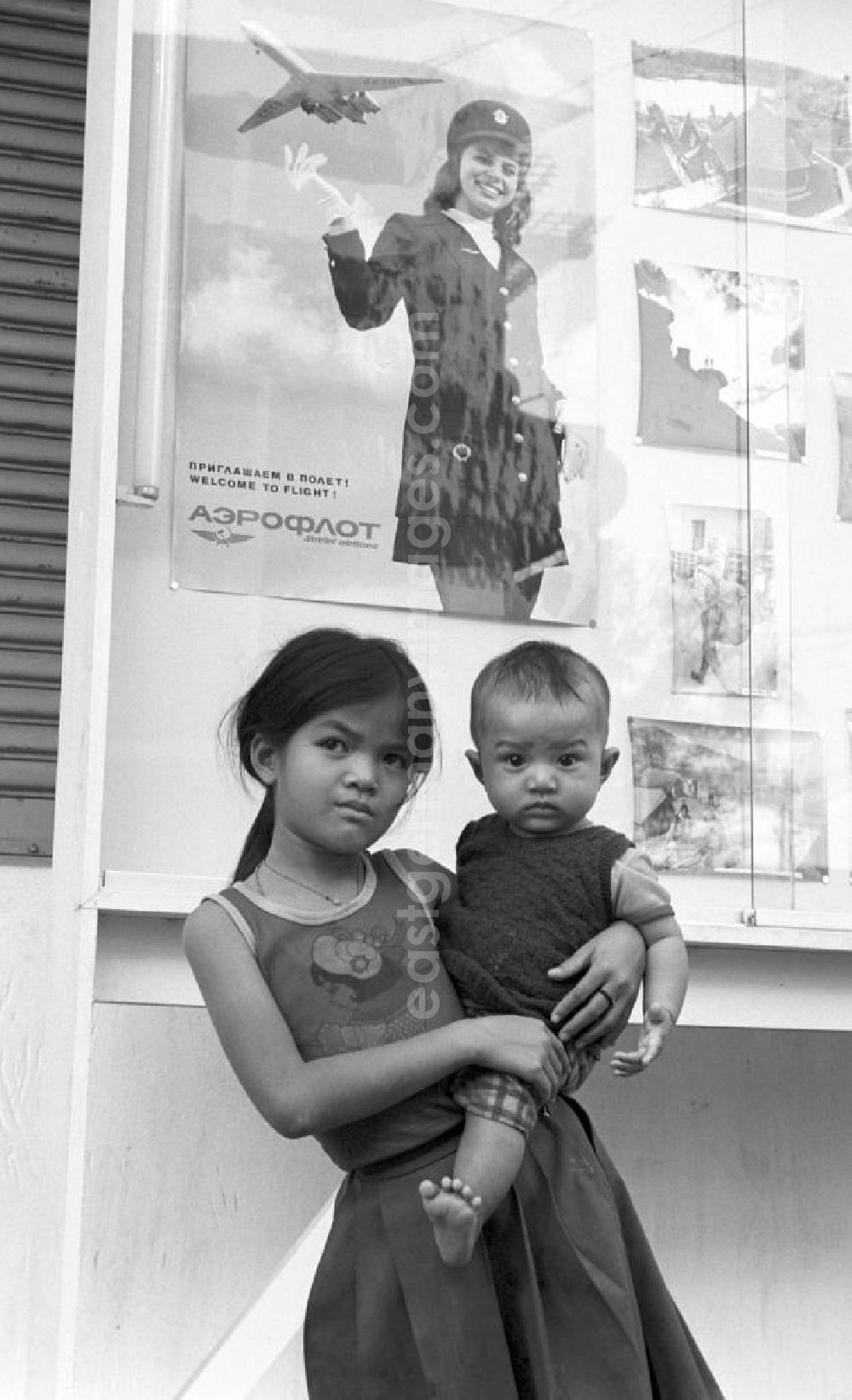 GDR image archive: Vientiane - Ein Mädchen steht mit einem Baby auf dem Arm vor einem Werbeplakat der russischen Fluggesellschaft Aeroflot in Vientiane in der Demokratischen Volksrepublik Laos.