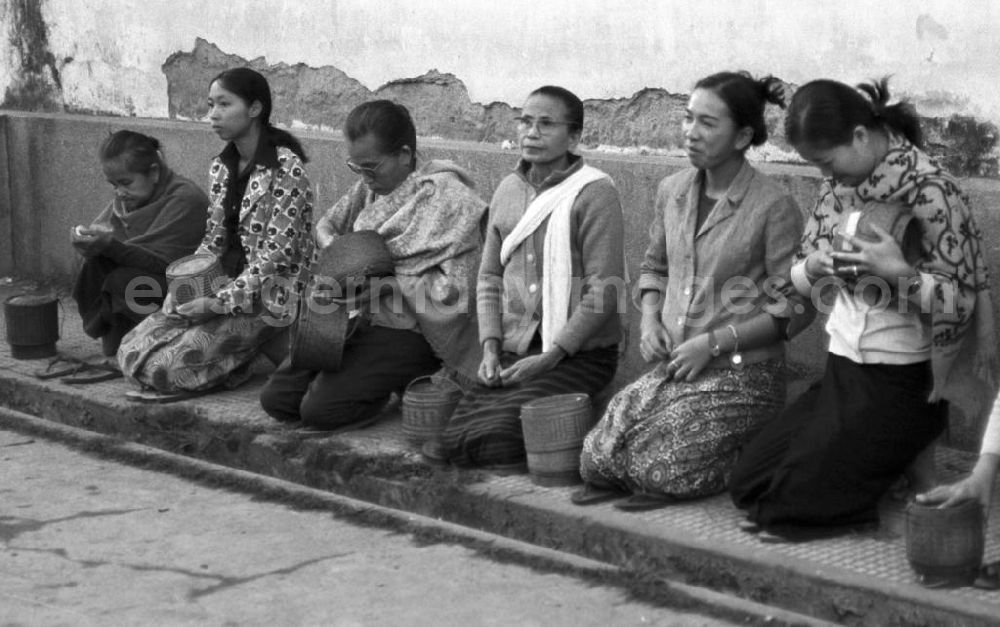 GDR image archive: Vientiane - Frauen sitzen am Straßenrand von Vientiane, der Hauptstadt der Demokratischen Volksrepublik Laos, und warten auf die Ankunft der Bettelmönche, die früh am Morgen durch die Straßen ziehen, um sich ihr Essen für den Tag zu erbetteln.