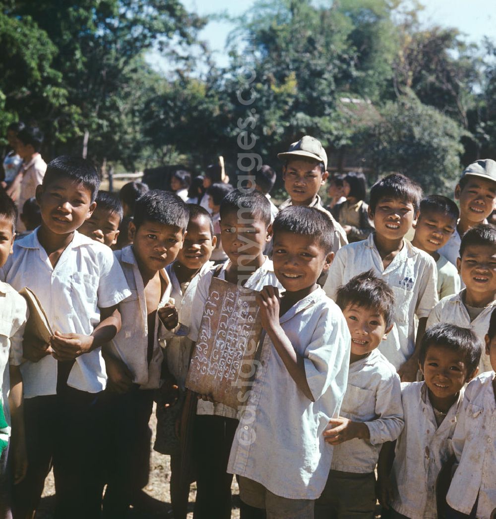 GDR photo archive: Vientiane - Ein Junge präsentiert dem Fotografen eine Schreibtafel auf dem Hof einer Schule in einem Dorf in der Demokratischen Volksrepublik Laos. Nach der Gründung der Volksrepublik Laos im Dezember 1975 wurde das Schulsystem von der neuen kommunistischen Regierung in Laos wieder aufgebaut, um dem in der Bevölkerung weit verbreiteten Analphabetismus entgegenzuwirken.
