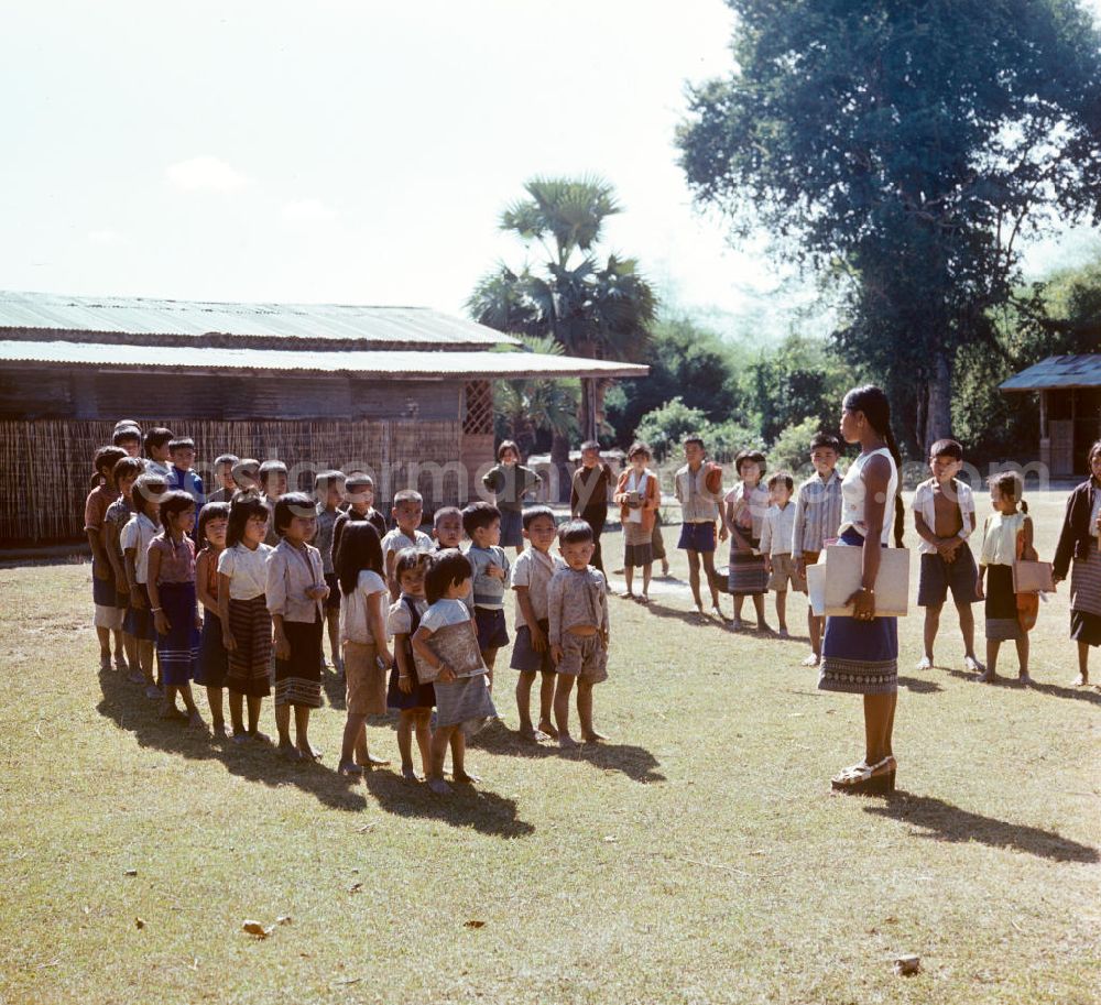 GDR picture archive: Vientiane - Kinder versammeln sich auf dem Hof einer Schule in einem Dorf in der Demokratischen Volksrepublik Laos. Nach der Gründung der Volksrepublik Laos im Dezember 1975 wurde das Schulsystem von der neuen kommunistischen Regierung in Laos wieder aufgebaut, um dem in der Bevölkerung weit verbreiteten Analphabetismus entgegenzuwirken.