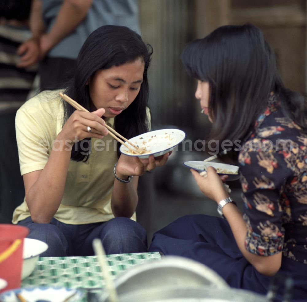 GDR photo archive: Vientiane - Zwei junge Frauen essen mit Stäbchen ein Reisgericht auf dem Markt von Vientiane in der Demokratischen Volksrepublik Laos.