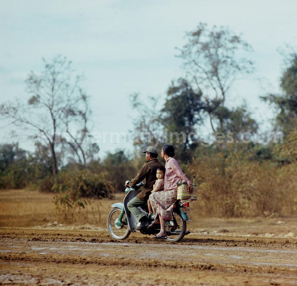 GDR photo archive: Vientiane - Familie auf einem Motorrad auf einer Straße in der Demokratischen Volksrepublik Laos.