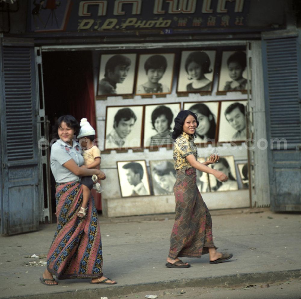 Vientiane: Zwei Frauen laufen mit einem Kind auf dem Arm an einem Fotogeschäft vorbei in Vientiane in der Demokratischen Volksrepublik Laos.