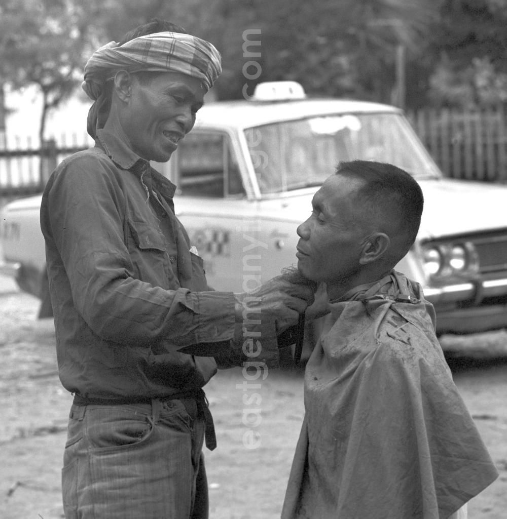 GDR photo archive: Vientiane - Auf einer Straße in Vientiane, der Hauptstadt der Demokratischen Volksrepublik Laos, läßt sich ein Mann seinen Bart rasieren.
