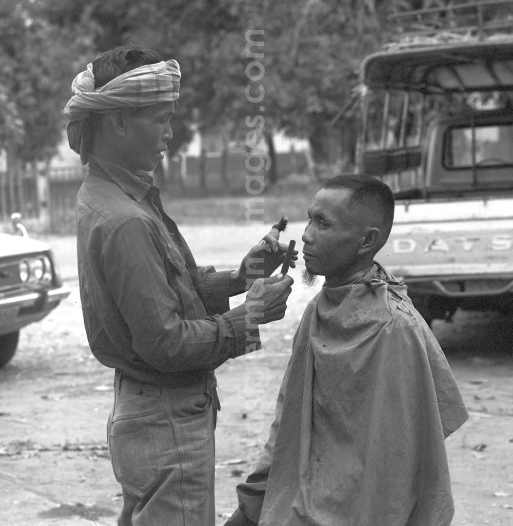 GDR picture archive: Vientiane - Auf einer Straße in Vientiane, der Hauptstadt der Demokratischen Volksrepublik Laos, läßt sich ein Mann seinen Bart rasieren.