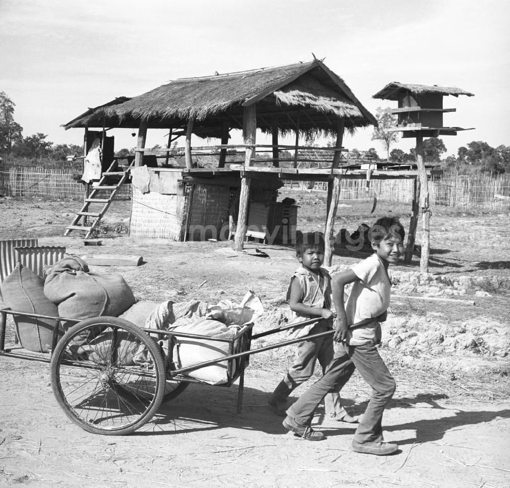Vientiane: Kinder ziehen einen Karren vor einer ärmlichen Hütte in einem Dorf in der Demokratischen Volksrepublik Laos.