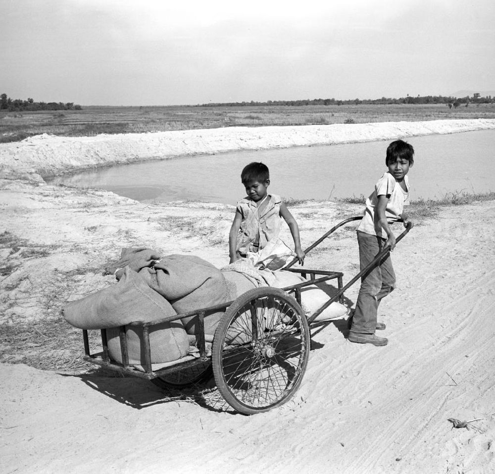 GDR photo archive: Vientiane - Kinder ziehen einen Karren auf einem Sandweg an einem Dorf in der Demokratischen Volksrepublik Laos.
