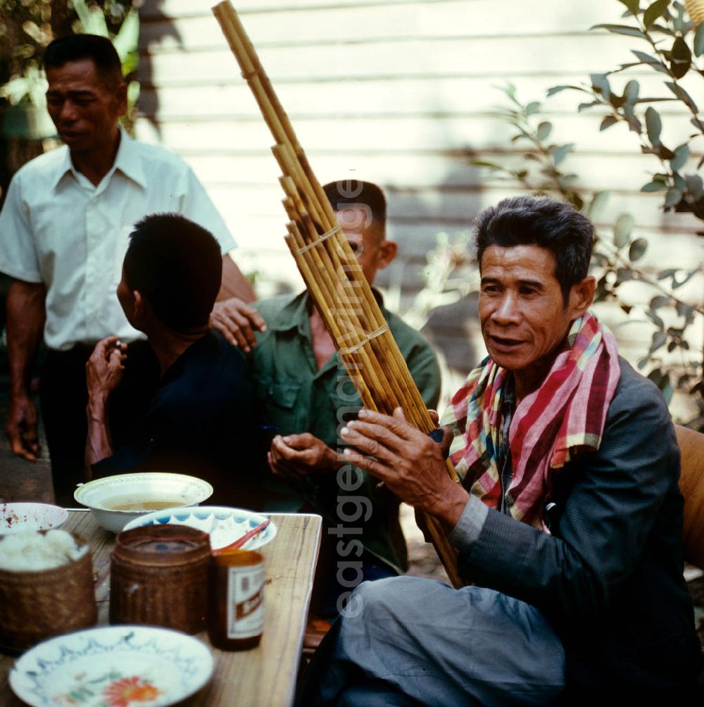 GDR picture archive: Vientiane - Ein Mann spielt auf einer Khaen zu einer Hochzeit in einem Dorf in der Demokratischen Volksrepublik Laos. Die asiatische Mundorgel ist das Nationalinstrument der Lao in Laos.