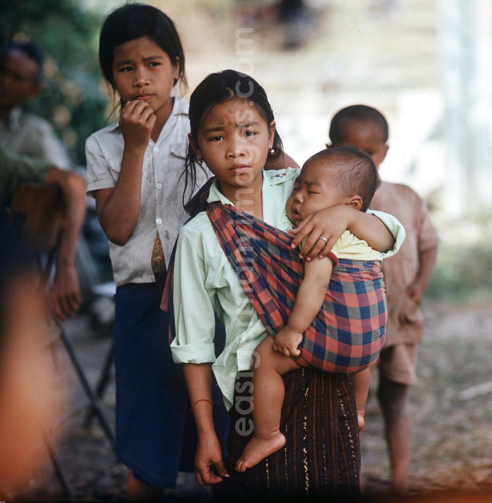 Vientiane: Mädchen mit Baby im Tragetuch in einem Dorf in der Demokratischen Volksrepublik Laos.