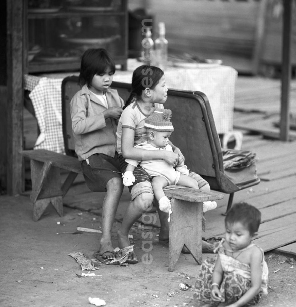 GDR image archive: Vientiane - Mädchen sitzen auf einer Bank vor ihrem Haus und flechten sich die Haare in Vientiane in der Demokratischen Volksrepublik Laos.