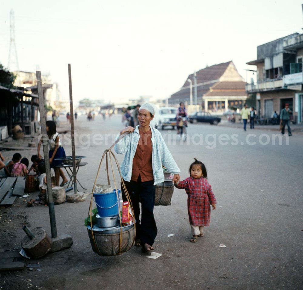 GDR photo archive: Vientiane - Frau mit geschulterten Körben und Kind an der Hand auf einer Straße in Vientiane in der Demokratischen Volksrepublik Laos.