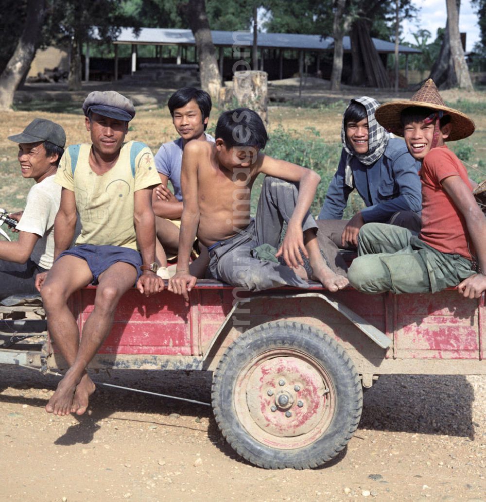 GDR picture archive: Nam Ngum - Auf dem Weg zur Feldarbeit amüsieren sich junge Männer auf dem Anhänger eines elektrischen Karrens in der Demokratischen Volksrepublik Laos.
